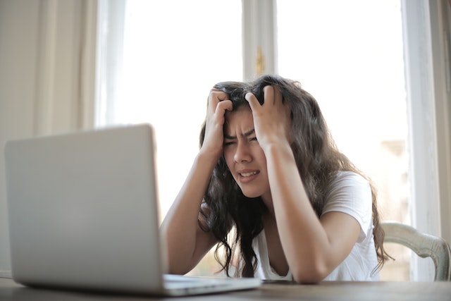 Stressad tjej sitter vid en dator med händerna i pannan