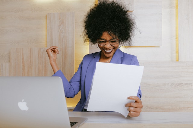 Glad kvinna med mörkt hår håller i ett papper vid ett skrivbort