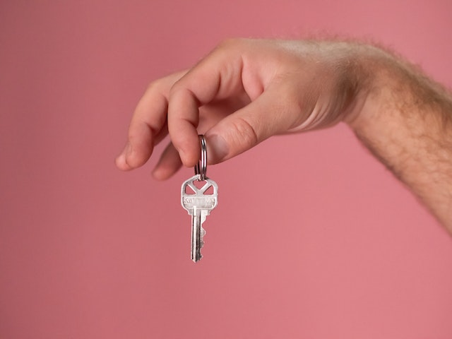 en hand som håller i en husnyckel med en rosa bakgrund