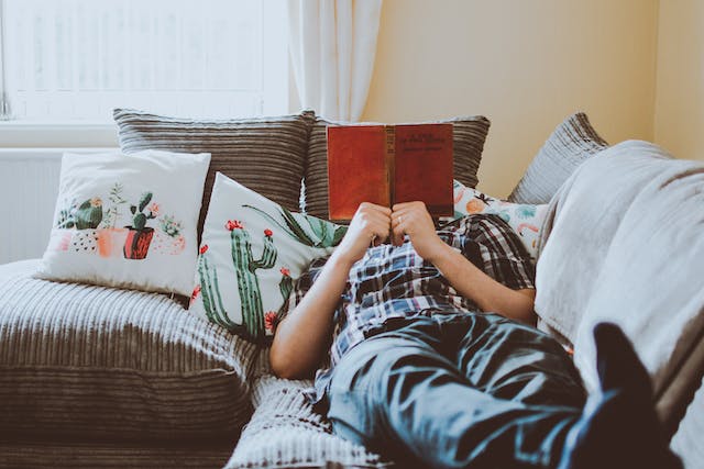 Person i rutig skjorta som ligger och läser en röd bok i en soffa